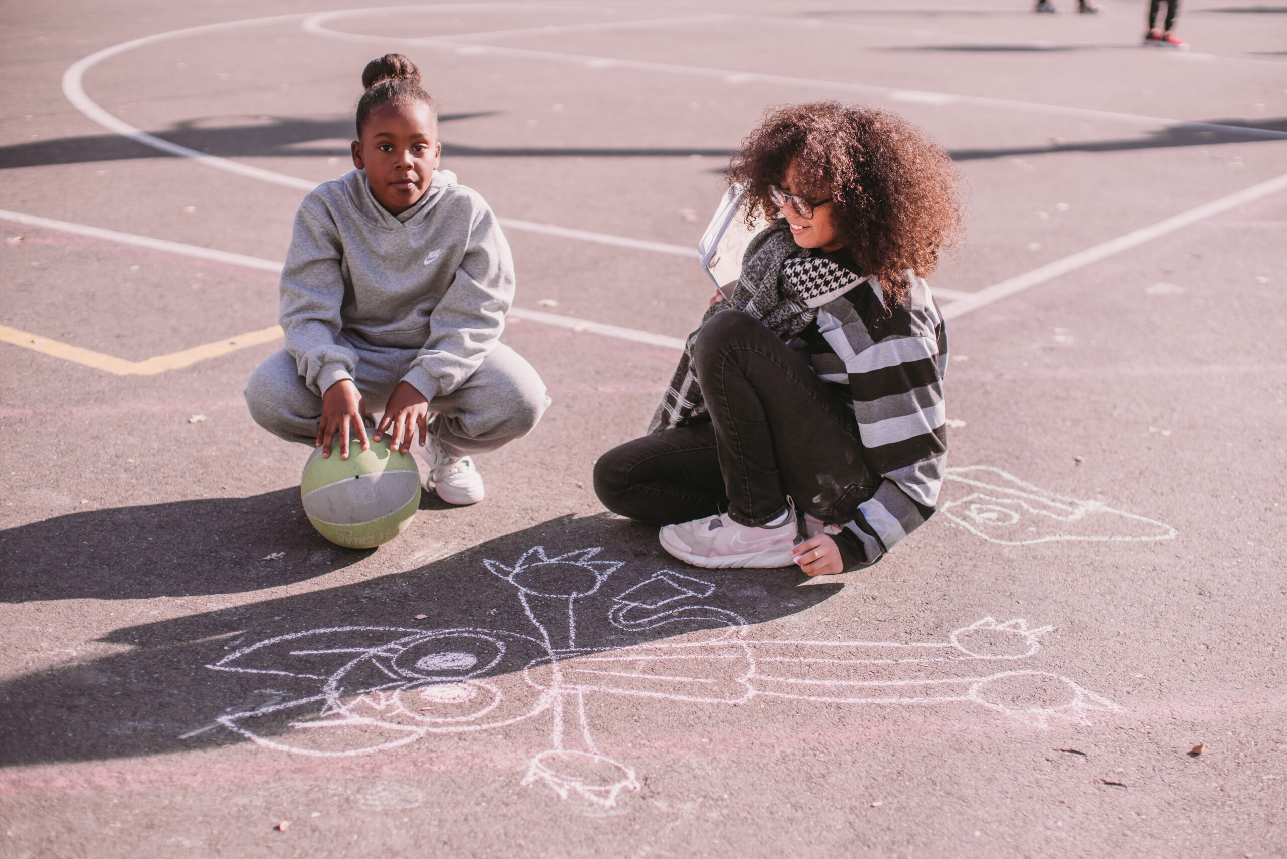 Two girls working on chalk drawing on the schools' blacktop.